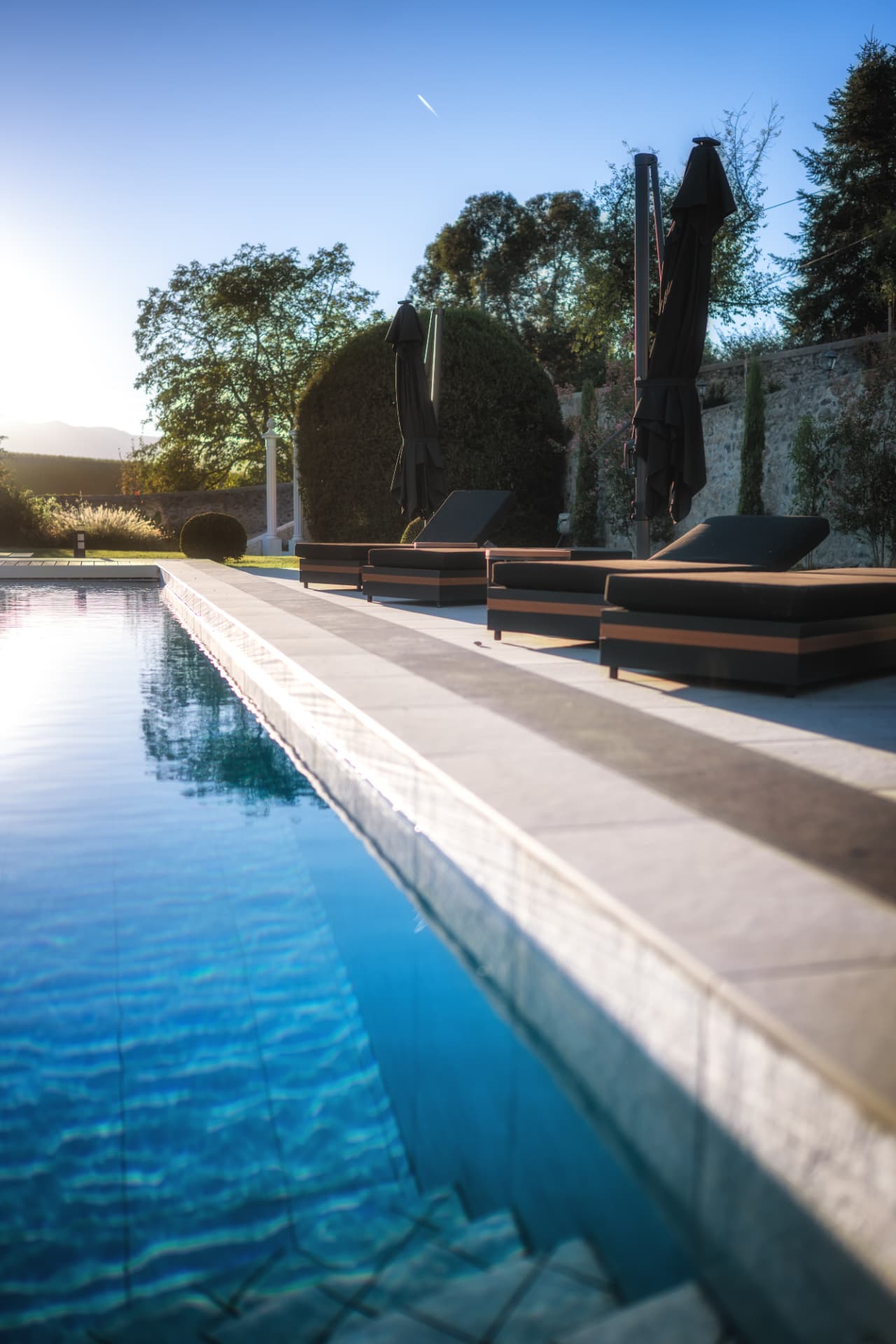 Transats et parasols au bord de la piscine chauffée du Château de Crâche au coucher du soleil