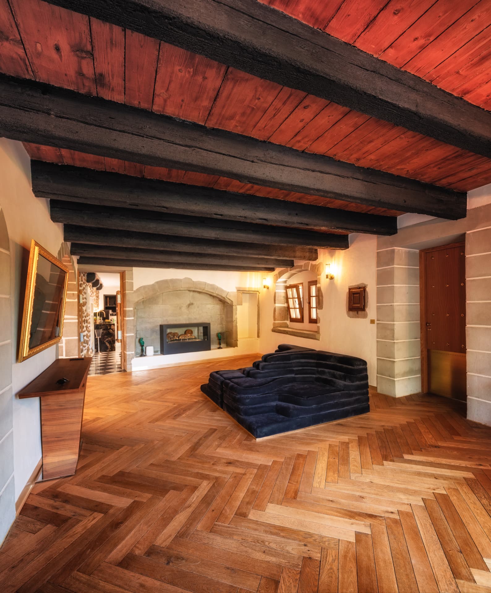 Salon sous les poutres anciennes du Château de Crâche, canapé de velours bleu nuit et cheminée de pierre