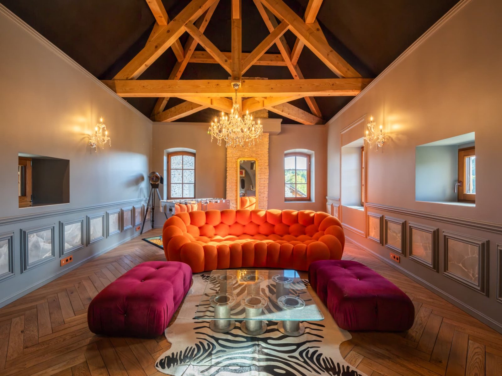 Salon sous les combles du Château de Crâche, charpente apparente, lustre et canapé orange Roche Bobois