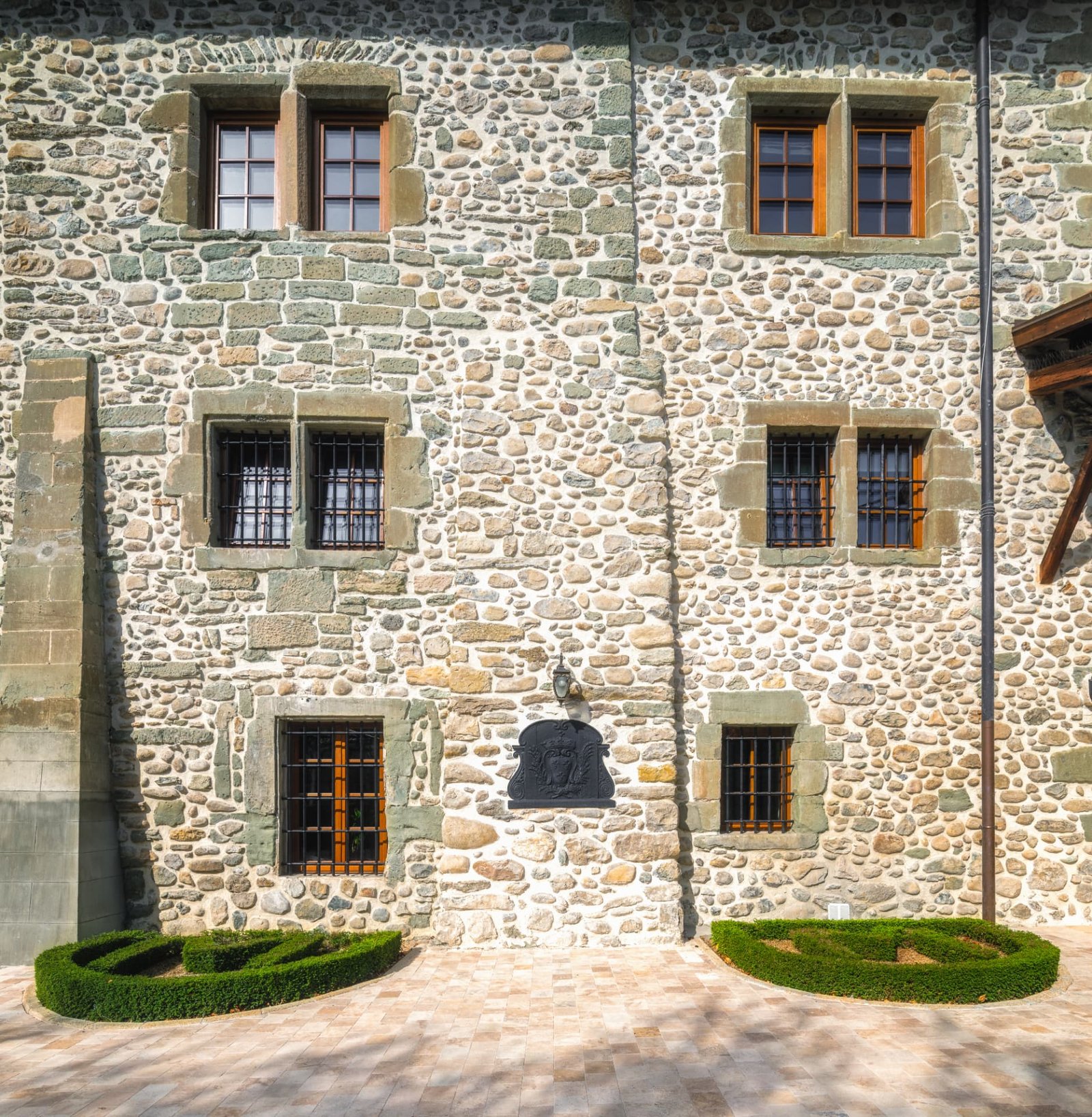Façade en galets du Château de Crâche, fenêtres à meneaux, grilles de fer forgé et armoiries