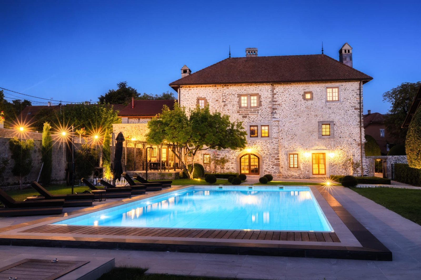 Château de Crâche en location exclusive — façade et piscine chauffée au crépuscule, Haute-Savoie