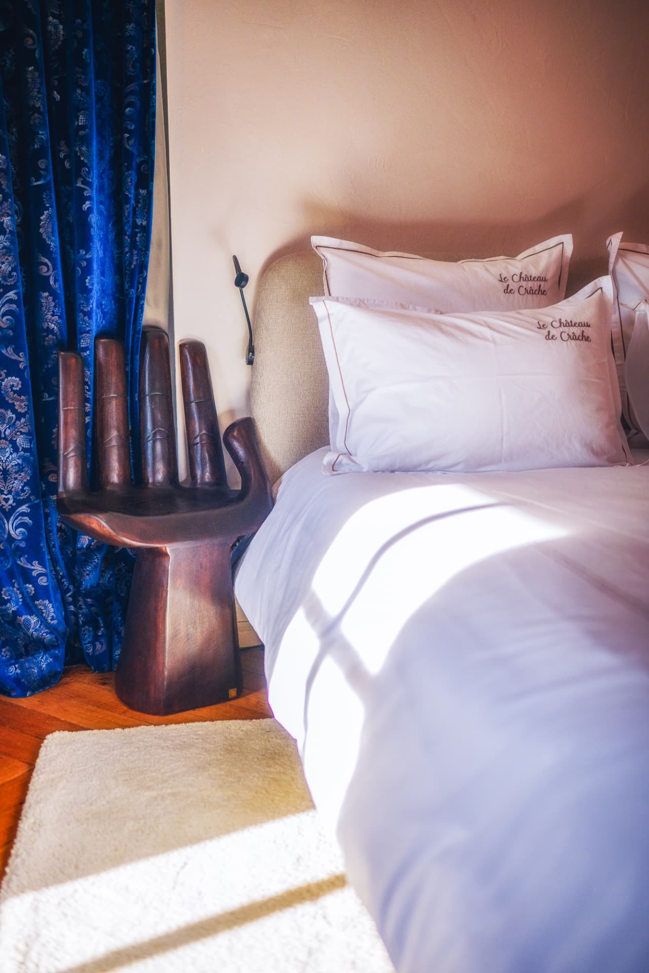 Détail de la Suite Léman avec linge brodé, rideaux bleus et fauteuil sculptural