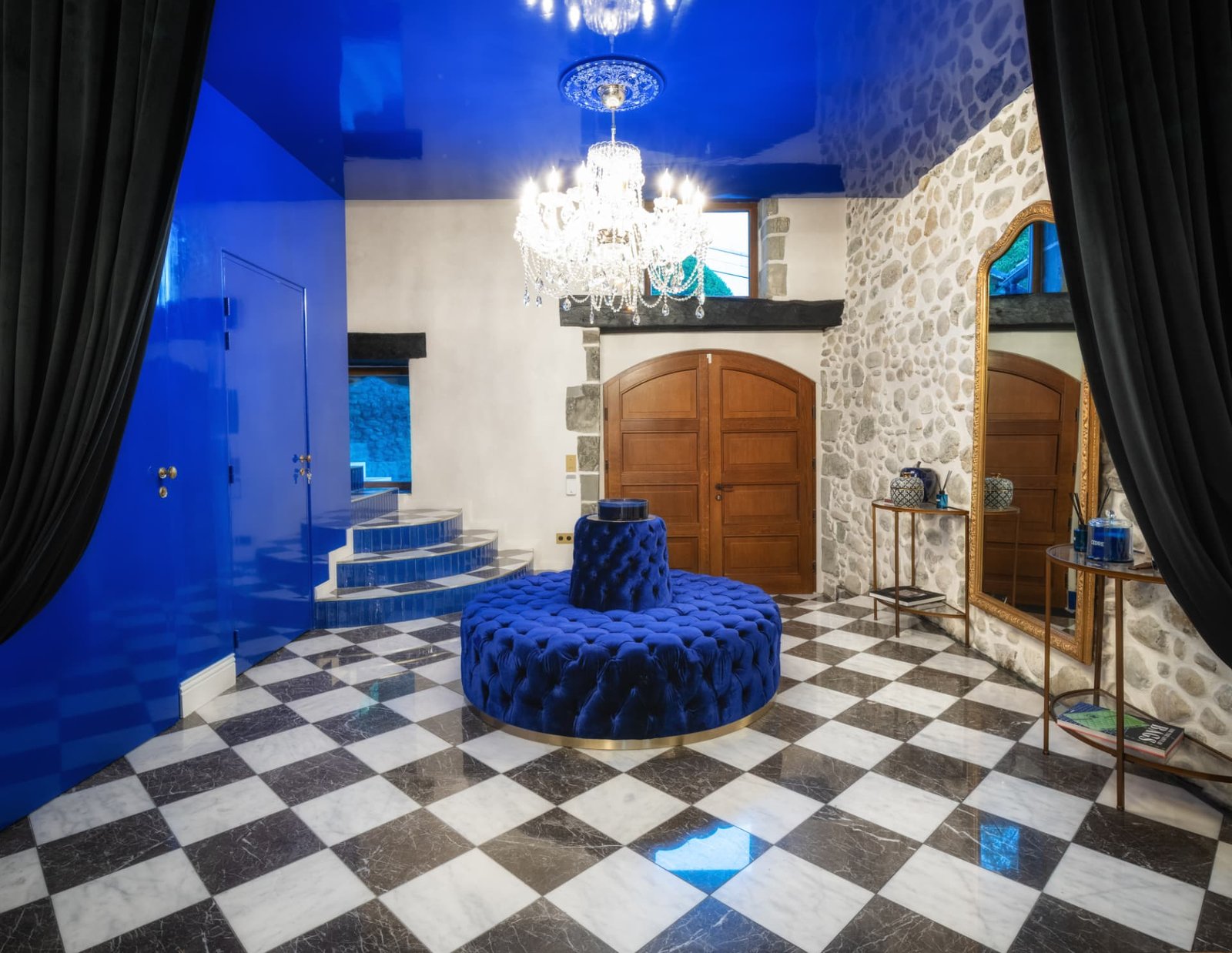 Hall d'entrée du Château de Crâche, canapé rond en velours bleu roi, lustre en cristal, plafond laqué bleu et sol en damier de marbre