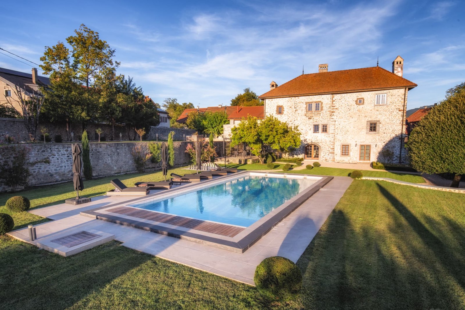 La piscine chauffée et la façade du Château de Crâche au soleil couchant, parc à la française