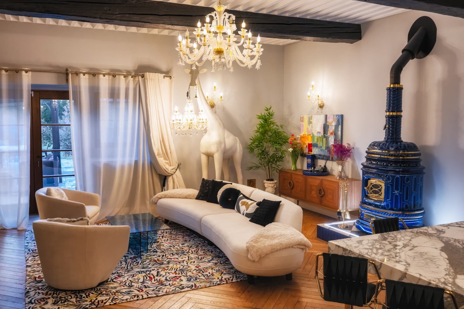 Salon sous poutres avec canapé courbe, lustres de cristal et poêle bleu, Château de Crâche
