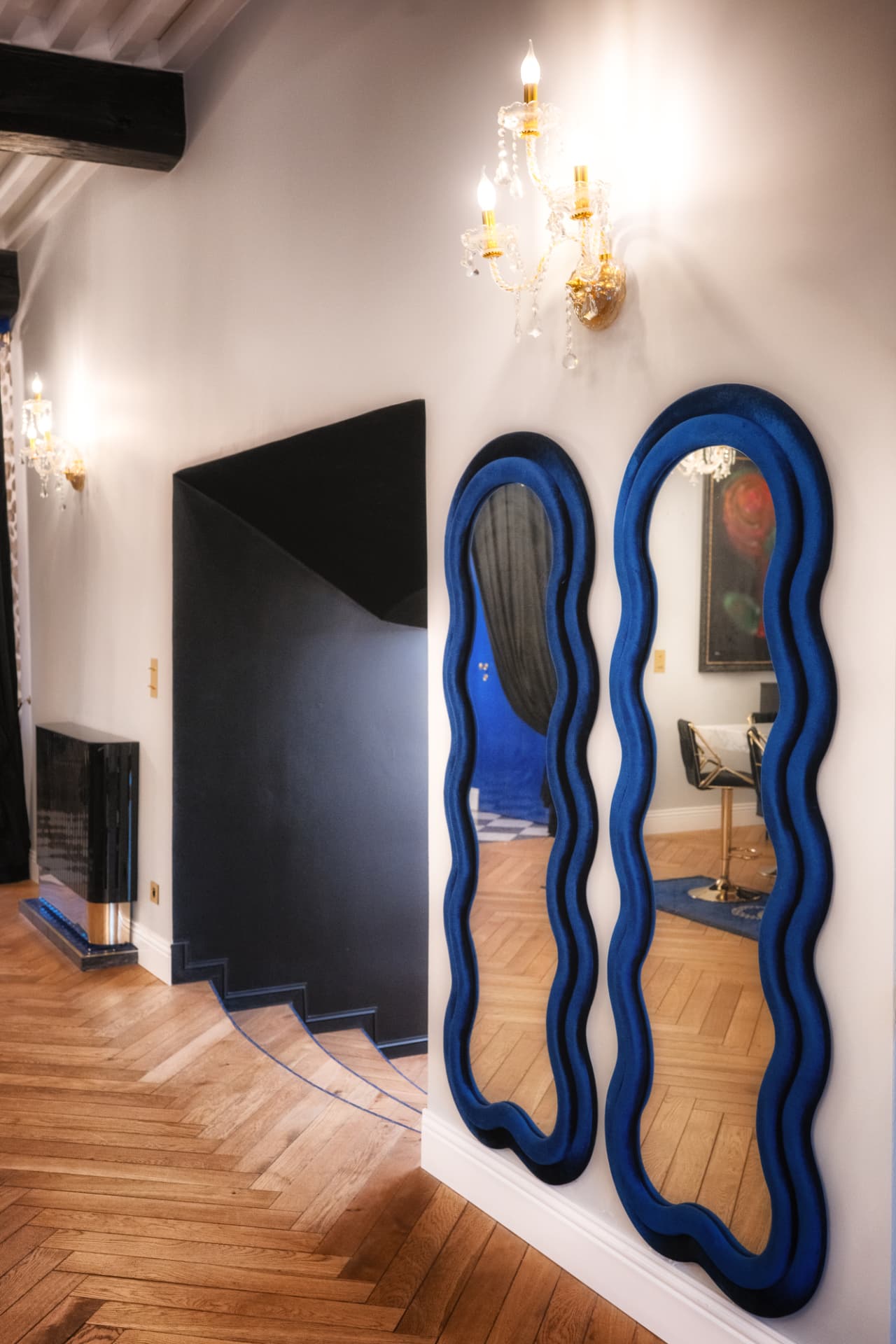 Deux miroirs ondulés en velours bleu dans un couloir à parquet chevrons, Château de Crâche